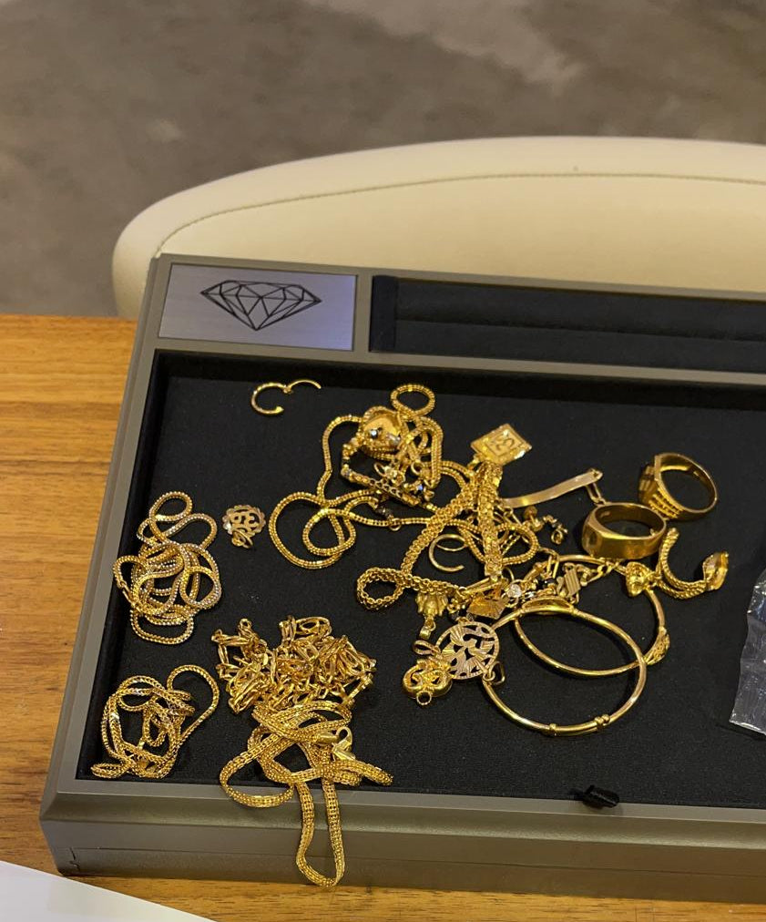 Set of gold earrings in a jewelry box on a wooden surface with papers and a pen.