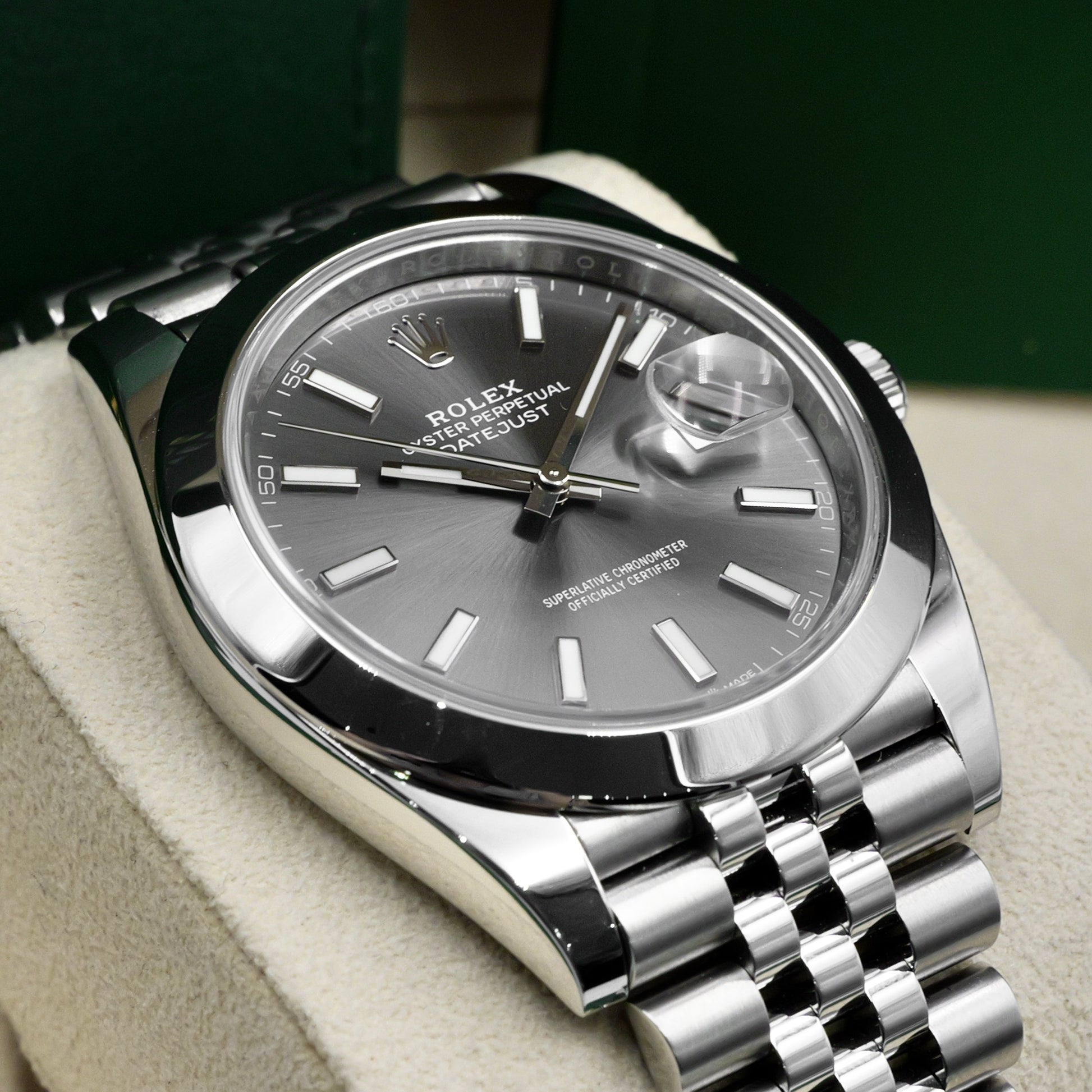 Silver Rolex watch with a dark face on a beige surface
