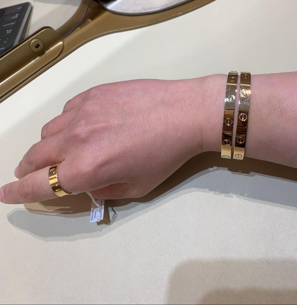 Hand with gold ring and bracelets on a white surface with a red object in the background