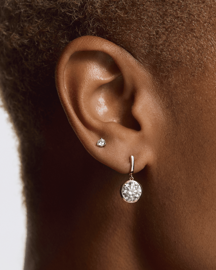 Close-up of an ear wearing a diamond earring with a plain background  yb jewellers yellow gold diamond drop earrings rubover setting